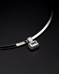A silver-toned torque necklace with a rectangular emerald-cut aquamarine gemstone pendant, displayed on a dark textured background.